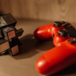 Close-up of a red game controller and 3D cube puzzle on a wooden surface.